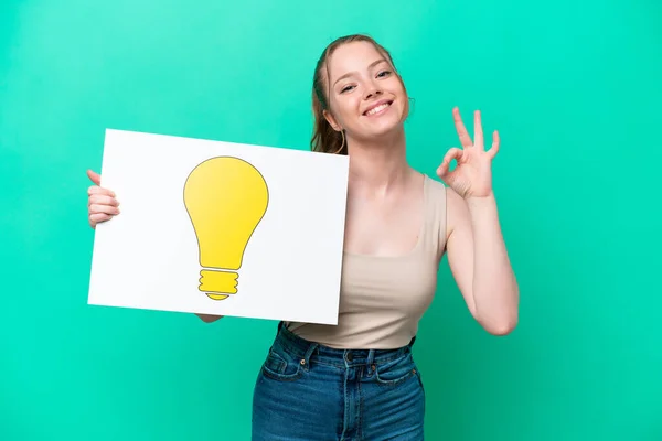 Young Caucasian Woman Isolated Green Background Holding Placard Bulb Icon — Photo