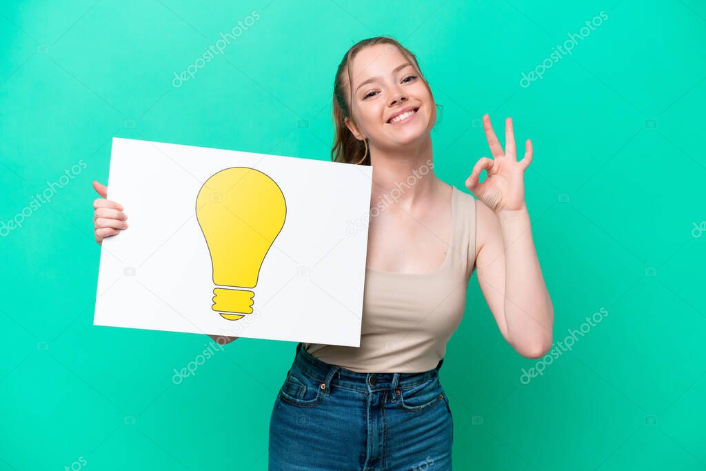 Young caucasian woman isolated on green background holding a placard with bulb icon with ok sign