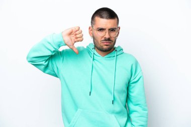 Beyaz arka planda izole genç beyaz adam olumsuz ifade ile baş parmağını göstermektedir