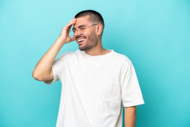 Kafkasyalı genç adam mavi arka planda izole edilmiş, çok gülümsüyor.