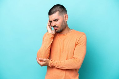 Kafkasyalı genç adam mavi arka planda izole edilmiş, baş ağrısı var.