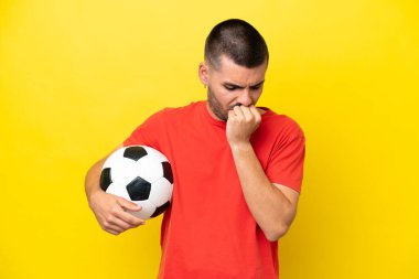 Young caucasian man playing soccer isolated on yellow background having doubts