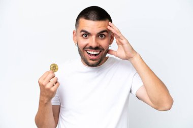 Beyaz arka planda, sürpriz bir ifadeyle izole edilmiş bitcoin tutan genç beyaz bir adam.