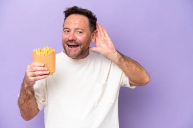 Orta yaşlı beyaz bir adam elinde kızarmış cipslerle Mor fırında izole edilmiş bir şekilde kulağına elini sürerek bir şeyler dinliyordu.