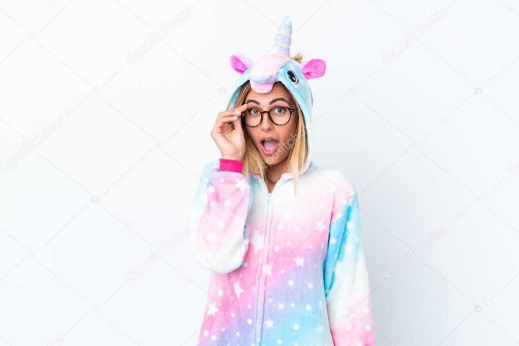 Blonde Uruguayan girl wearing a unicorn pajama isolated on white background with glasses and surprised
