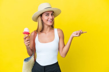 Sarışın Uruguaylı kız, yaz mevsiminde sarı arka planda izole edilmiş dondurma tutuyor.