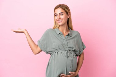 Genç Uruguaylı kadın mavi arka planda izole edilmiş hamile ve bir şey sunuyor.