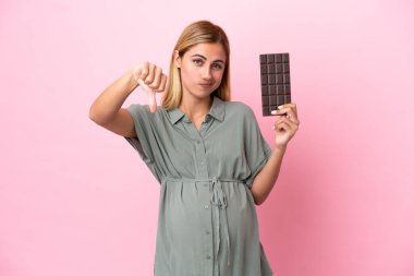 Genç Uruguaylı kadın mavi arka planda izole edilmiş hamile ve elinde çikolatayla kötü sinyal veriyor.