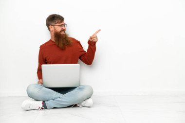 Dizüstü bilgisayarlı, beyaz arka planda izole edilmiş genç, beyaz bir beyaz adam. Parmağını yana uzattı ve bir ürün sundu.