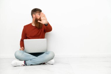 Beyaz arka planda dizüstü bilgisayarı olan genç, beyaz bir adam durdurma hareketi yapıyor ve hayal kırıklığına uğruyor.