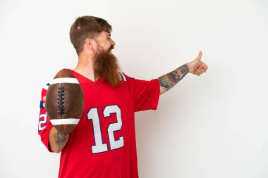 Beyaz arka planda ragbi oynayan Kafkas 'lı genç adam baş parmak hareketi yapıyor.