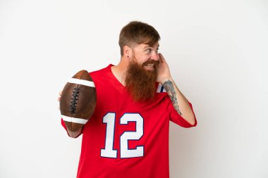 Beyaz arka planda ragbi oynayan Kafkasyalı genç bir adam elini kulağına koyarak bir şeyler dinliyor.