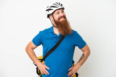 Termal sırt çantalı genç beyaz adam, beyaz arka planda, kolları kalçasında ve gülümseyerek poz veriyor.