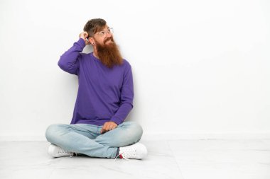 Beyaz arka planda izole bir şekilde yerde oturan Kafkasyalı genç adamın şüpheleri vardı ve kafası karışmıştı.