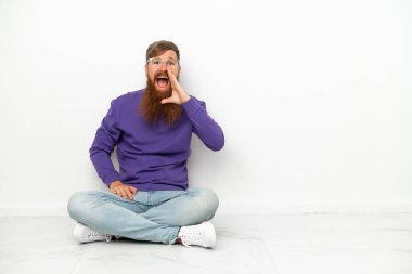 Beyaz arka planda izole bir şekilde yerde oturan beyaz tenli genç adam ağzı açık bağırıyordu.