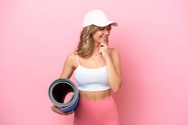 Genç sporcu kadın yoga derslerine giderken elinde minderle yan tarafa bakıyor ve gülümsüyor.