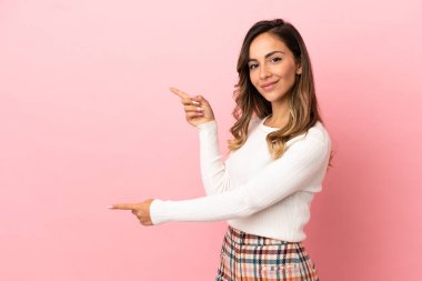 İzole edilmiş arka planda genç bir kadın parmağını yana uzatarak bir ürün sunuyor.