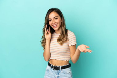 İzole edilmiş mavi arka planı olan genç bir kadın cep telefonuyla sohbet ediyor.