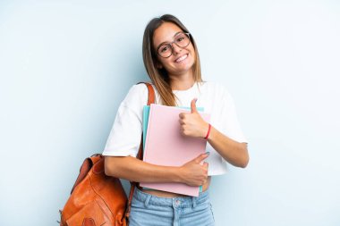 Mavi arka planda izole edilmiş genç bir bayan baş parmak hareketi yapıyor.