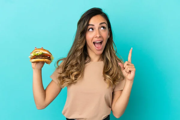 Młoda Kobieta Trzyma Hamburgera Nad Odosobnionym Tłem Myśląc Pomyśle Wskazującym — Zdjęcie stockowe
