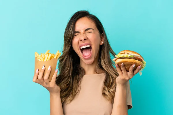 Young woman holding fried chips  and burger over isolated background