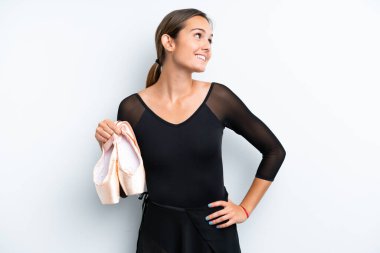 Beyaz arka planda izole bir şekilde dans eden beyaz kadın kolları kalçasında poz veriyor ve gülümsüyor.