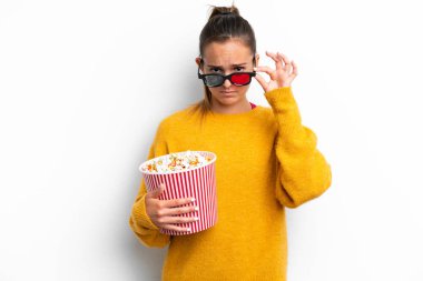 Beyaz arka planda izole edilmiş beyaz bir kadın 3D gözlüklü ve elinde koca bir kova patlamış mısırla şaşırdı.