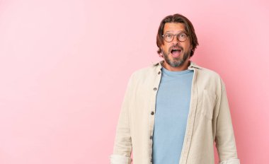 Yaşlı Hollandalı adam, pembe arka planda izole edilmiş, şaşırmış bir yüz ifadesi var.