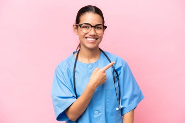 Pembe arka planda izole edilmiş genç Kolombiyalı hemşire bir ürünü sunmak için kenarı işaret ediyor.