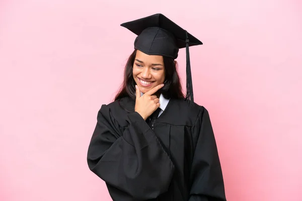 Young university Colombian woman graduate isolated on pink background looking to the side