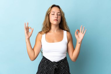 Zen pozunda mavi arka planda izole edilmiş genç sarışın kadın.