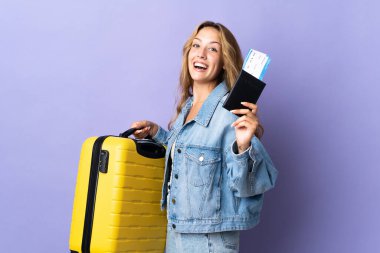 Genç sarışın kadın, mor arka planda izole edilmiş. Tatilde, bavullu ve pasaportlu.