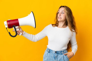 Sarı arka planda izole edilmiş genç sarışın kadın elinde stresli bir ifadeyle megafon tutuyor.