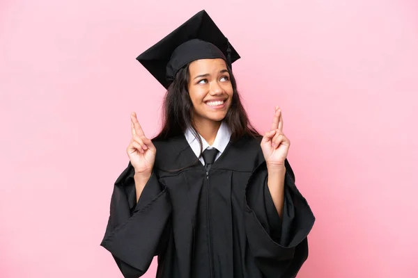 Young university Colombian woman graduate isolated on pink background with fingers crossing