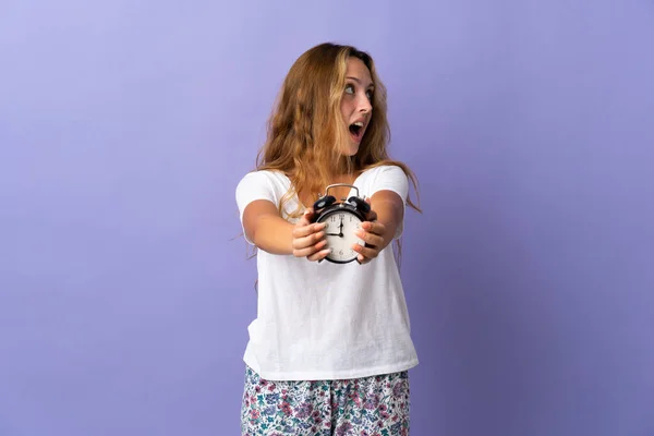 Young Blonde Woman Isolated Purple Background Pajamas Holding Clock — Φωτογραφία Αρχείου