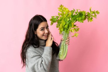 Mavi arka planda izole edilmiş kereviz tutan beyaz bir kadın bir şeyler fısıldıyor.