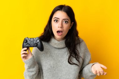 Woman playing with a video game controllerisolrted on yellow background with shocked facial expression