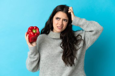 Mavi arka planda karabiber tutan beyaz bir kadın. Şüpheleri var ve kafası karışık.