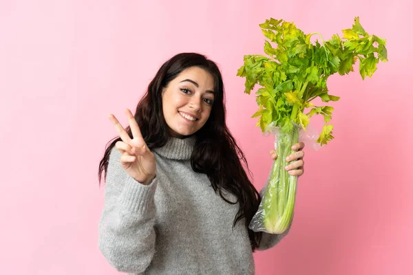 Jovem Caucasiana Segurando Aipo Isolado Fundo Azul Sorrindo Mostrando Sinal — Fotografia de Stock