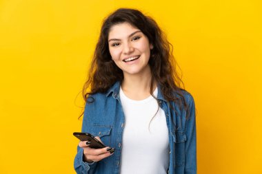 Genç Rus kız cep telefonu kullanarak sarı arka planda izole edilmiş.