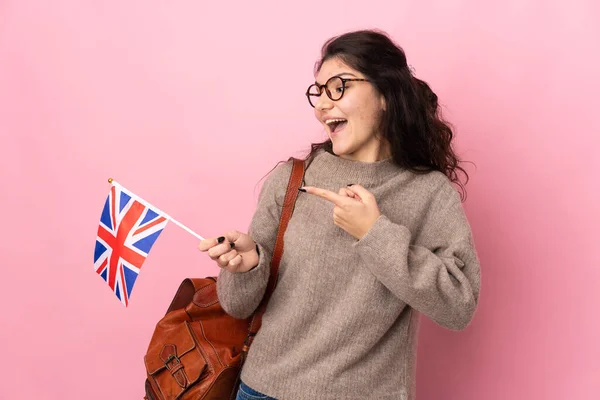 Young Russian woman holding an United Kingdom flag isolated on pink background intending to realizes the solution while lifting a finger up