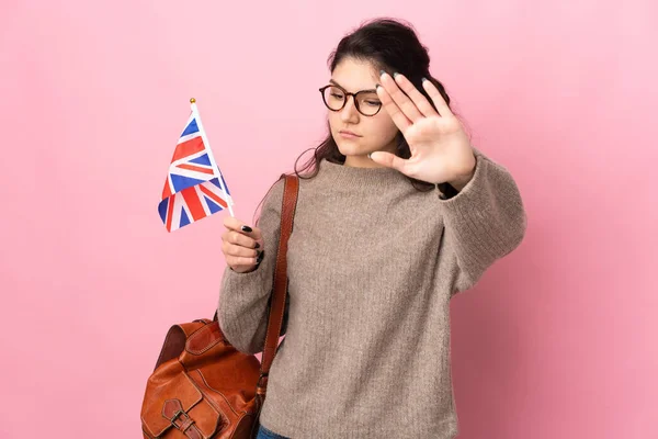 若いロシアの女性はピンクの背景に隔離された英国の旗を持っている停止ジェスチャーと失望を作る — ストック写真
