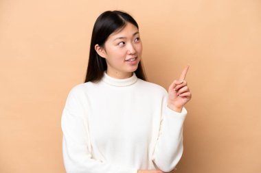 Bej arka planda izole edilmiş genç Çinli kadın harika bir fikre işaret ediyor.