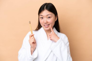 Genç Çinli kadın bej arka planda izole edilmiş diş fırçası ve mutlu bir ifadeyle.