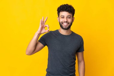 Faslı genç adam sarı arka planda izole edilmiş. Parmaklarıyla işaret veriyor.
