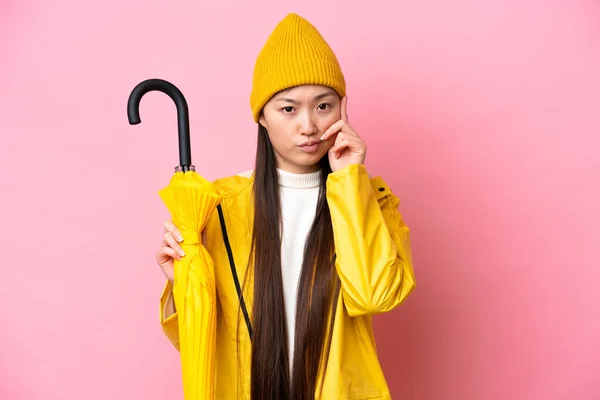 Young Chinese Woman Rainproof Coat Umbrella Isolated Pink Background Thinking — Stockfoto
