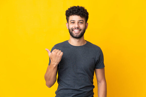 Young Moroccan man isolated on yellow background pointing to the side to present a product