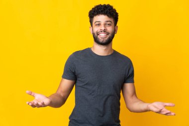 Sarı arka planda izole edilmiş genç Faslı adam mutlu ve gülümsüyor.