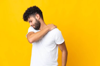 Genç Faslı bir adam sarı arka planda izole edilmiş omuz ağrısından muzdarip.
