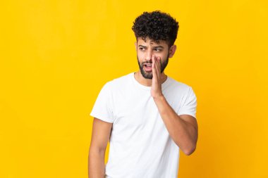 Genç Faslı bir adam sarı arka planda izole edilmiş. Yan tarafa bakarken sürpriz hareketlerle bir şeyler fısıldıyor.